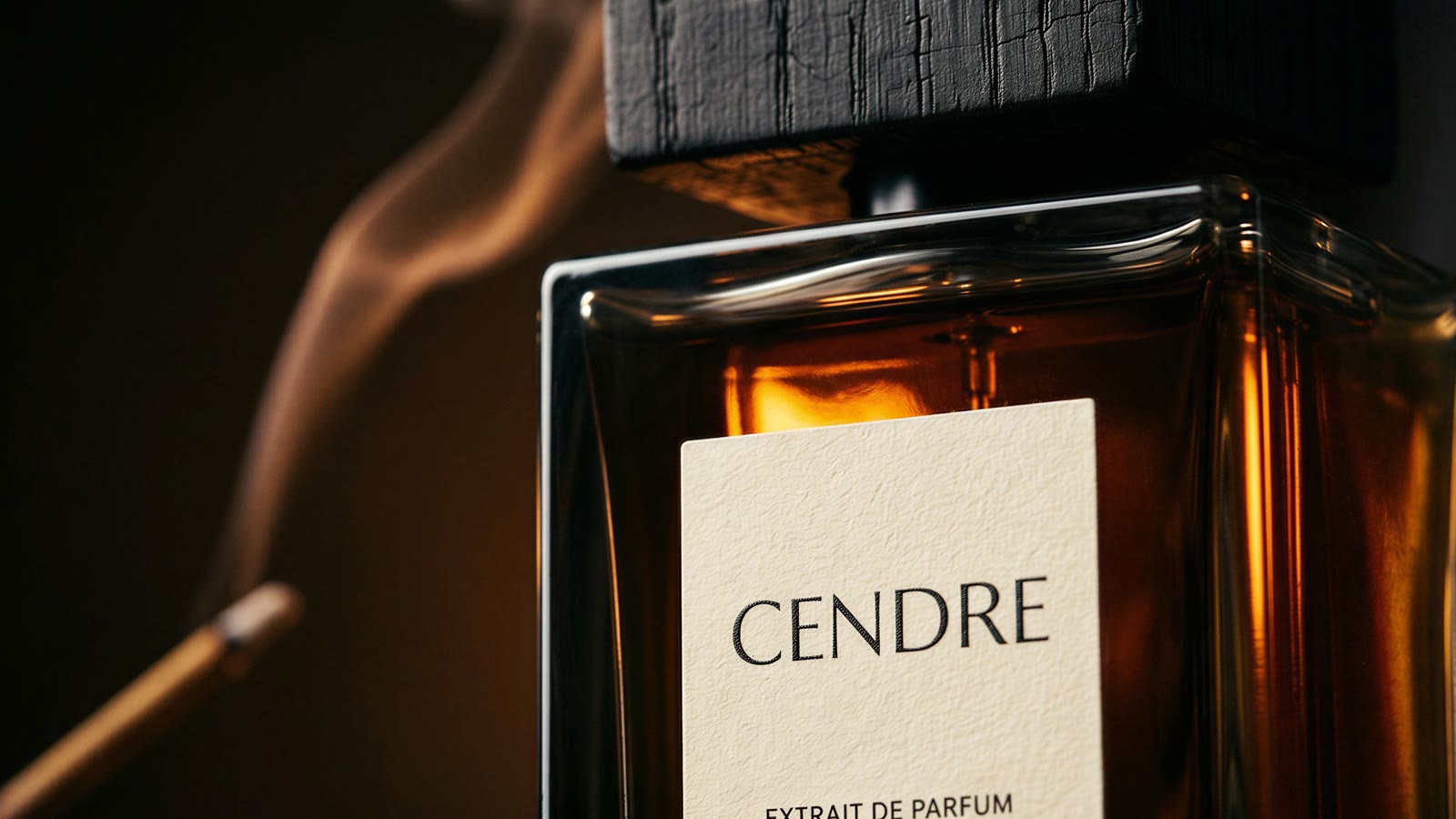 Macro of a cream paper label reading CENDRE, Extrait de Parfum, under a cracked charred cap
