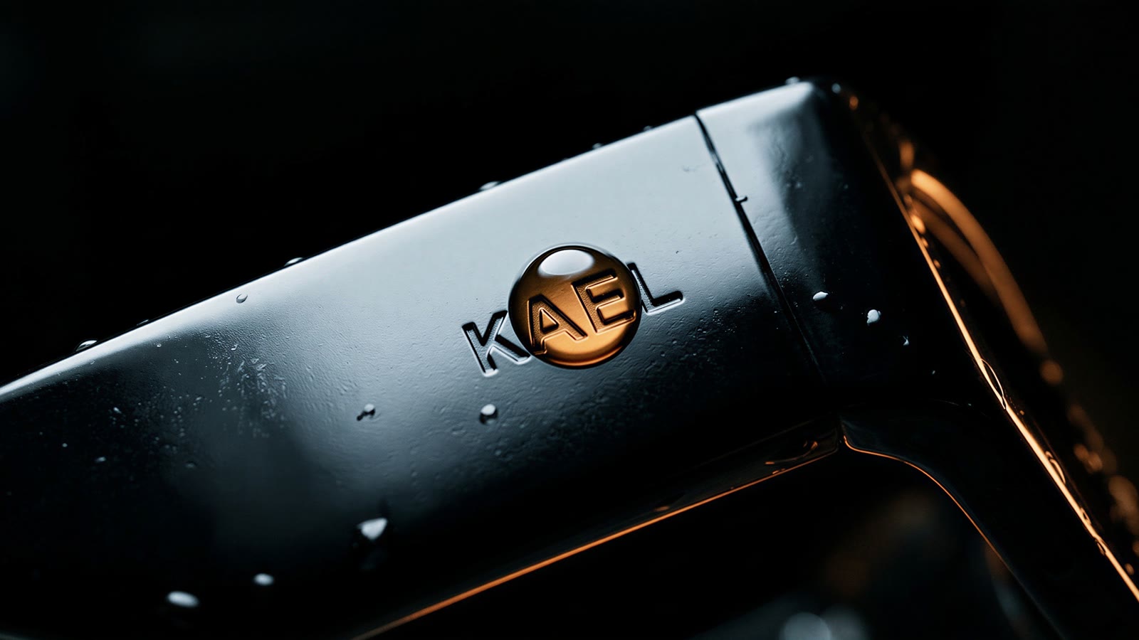 Extreme macro of KAEL debossed in a glossy black temple arm with a raindrop on the letters