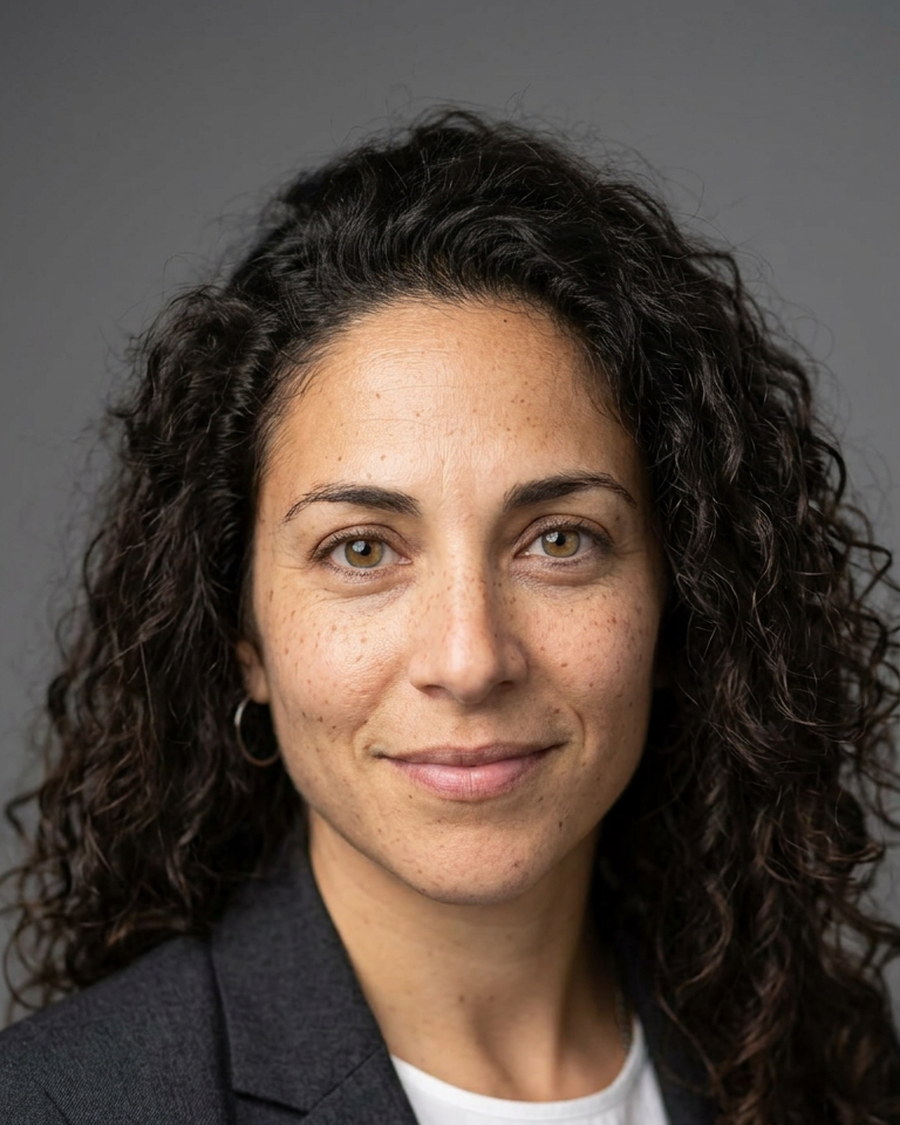 Corporate headshot of a woman with curly hair against a grey studio background
